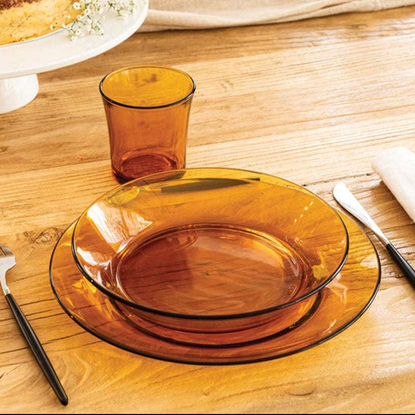 Duralex USA Lys Amber Glass Tumbler set of 6 displayed with matching amber plates on a wooden table, showcasing elegant drinkware in a stylish setting.