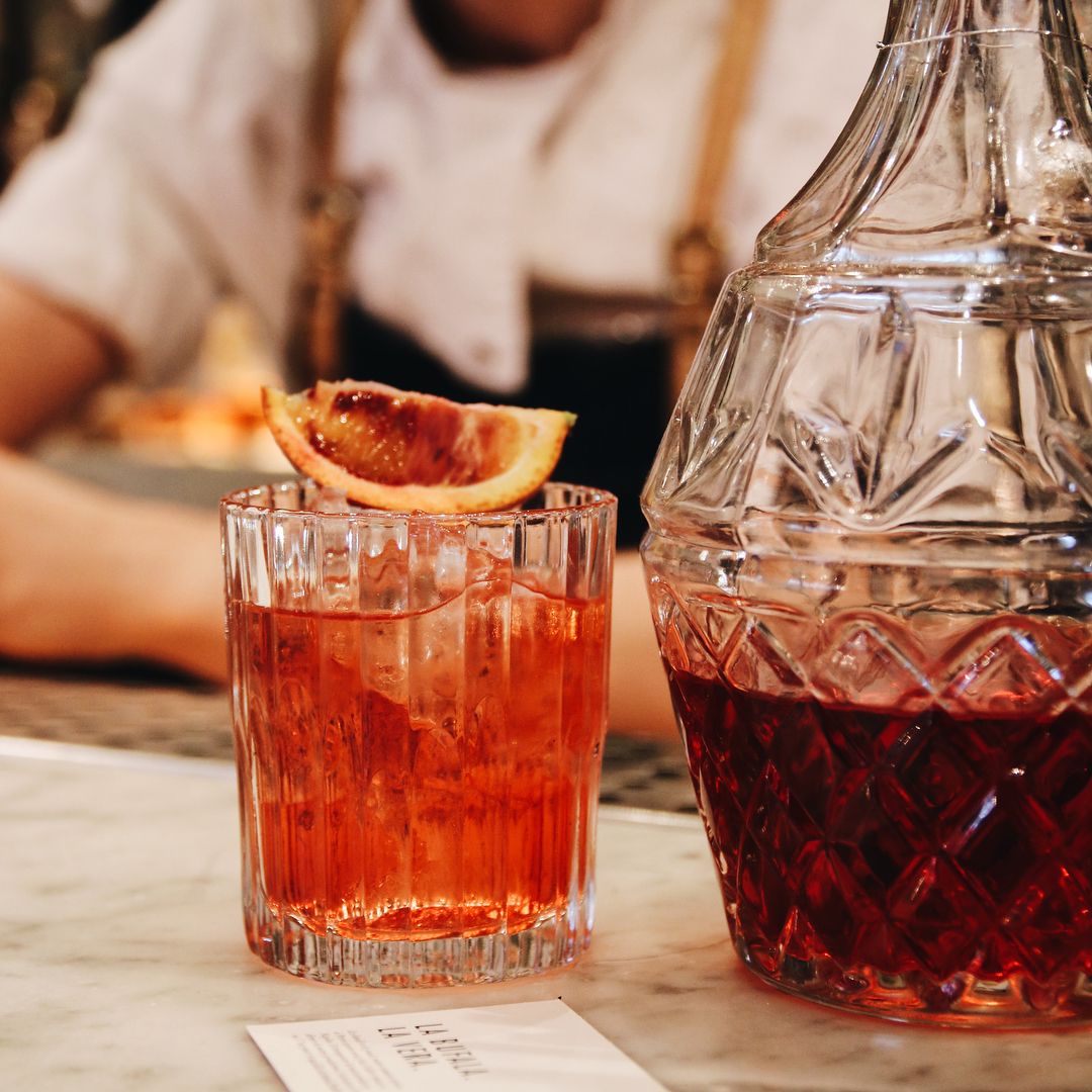 Manhattan Old Fashioned Glass - Set of 6 by Duralex featuring a vibrant cocktail garnished with a slice of citrus.