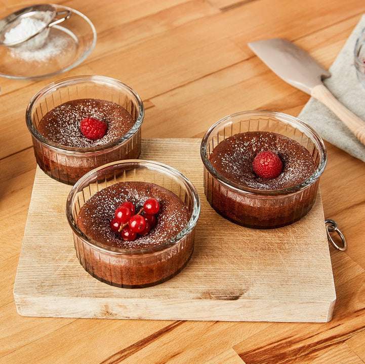 Three Ovenchef® Clear Tempered Glass Ramekins by Duralex filled with chocolate desserts, beautifully presented on a wooden board.