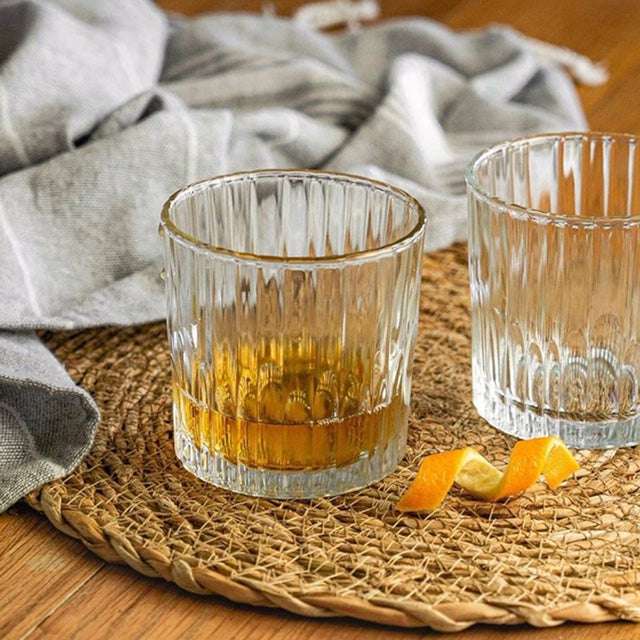 Manhattan Old Fashioned Glass - Set of 6 by Duralex, featuring two glasses on a woven placemat with orange peel garnish.