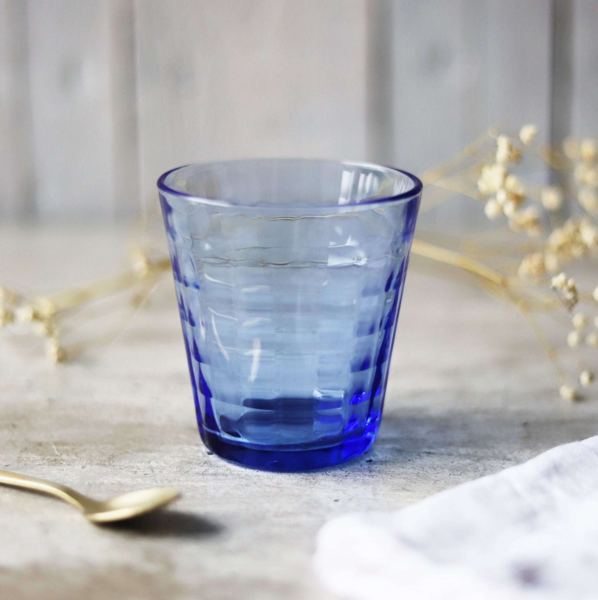 Prisme Marine Glass Tumbler by Duralex, featuring a blue glass tumbler with a unique faceted design, elegantly placed on a neutral background.
