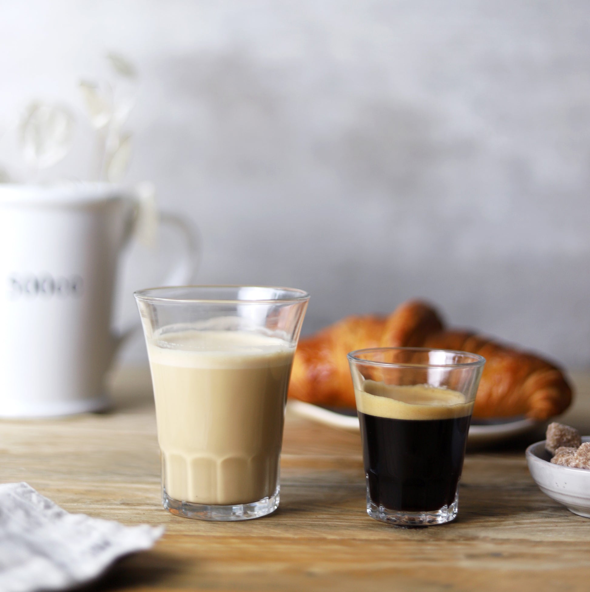 Two drinking glasses on a table one has milk the other has coffee 