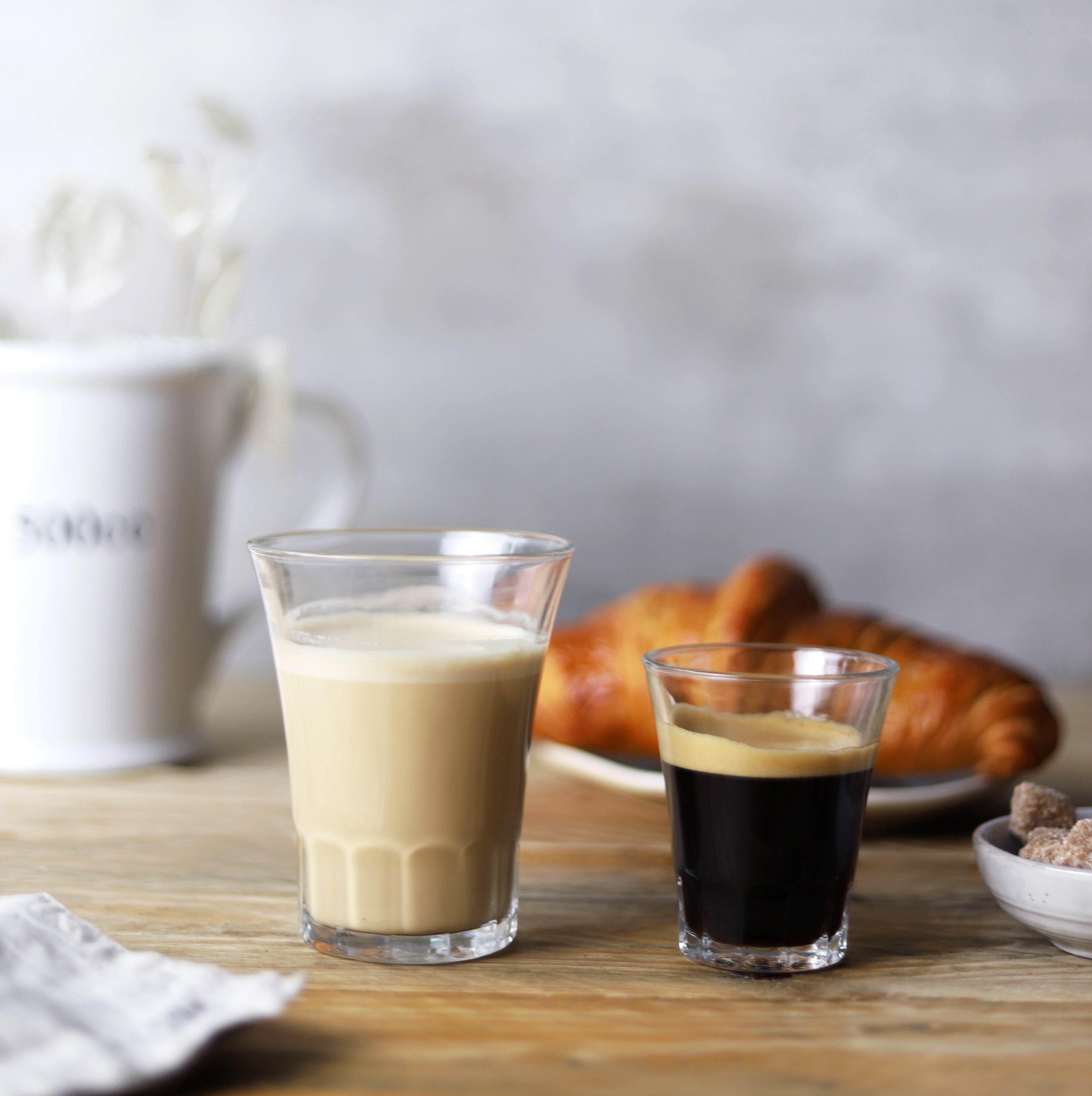 Two drinking glasses on a table one has milk the other has coffee 