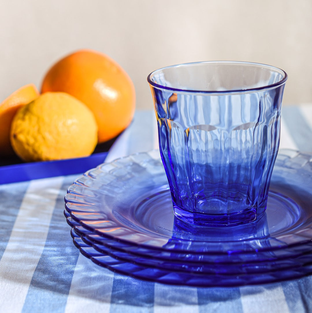 Le Picardie® Marine Glass Tumbler on a blue striped tablecloth with fresh fruits, designed by Duralex.